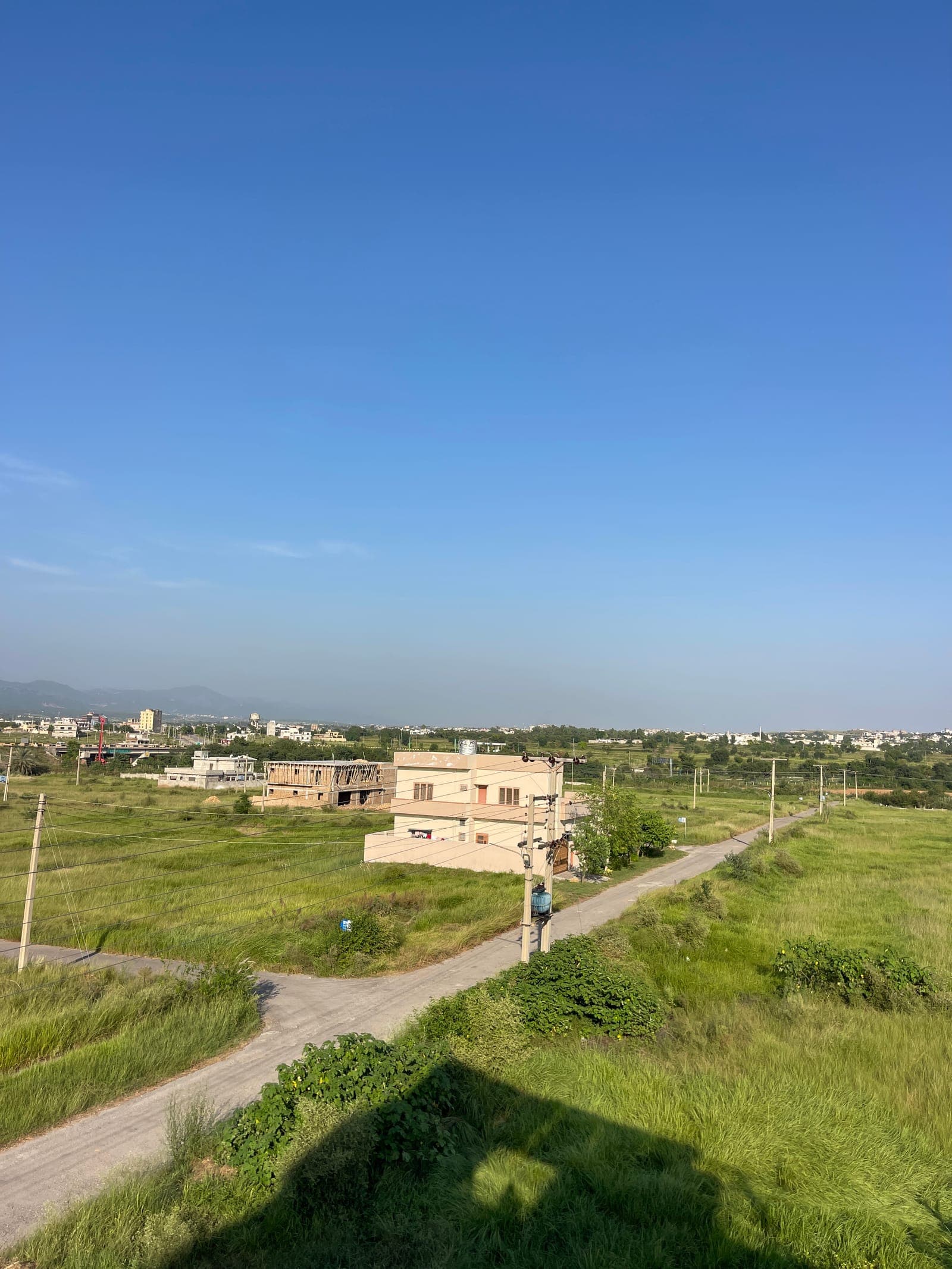 Open plots and a newly built house along a road in AWT D-18, Islamabad